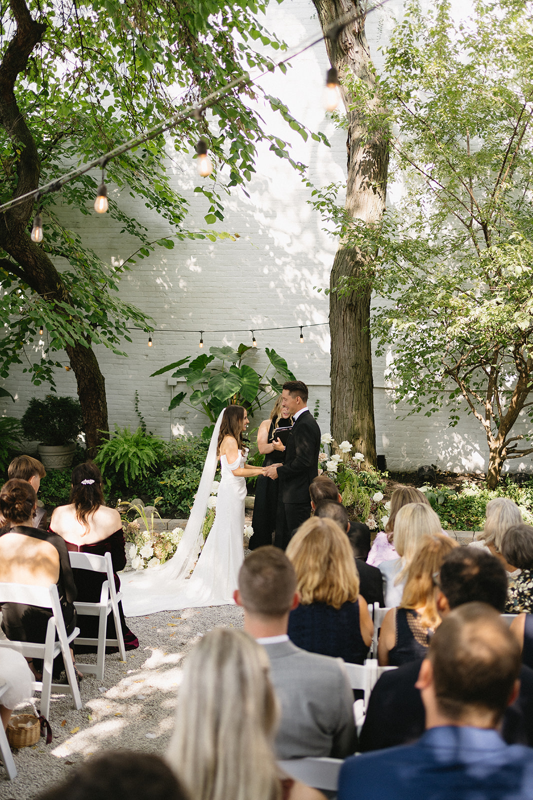 Bride and groom holding hands during outdoor summer wedding in Cleveland with greenery in the background